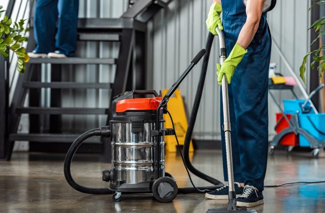 cropped view of cleaner in uniform cleaning floor with vacuum cleaner
